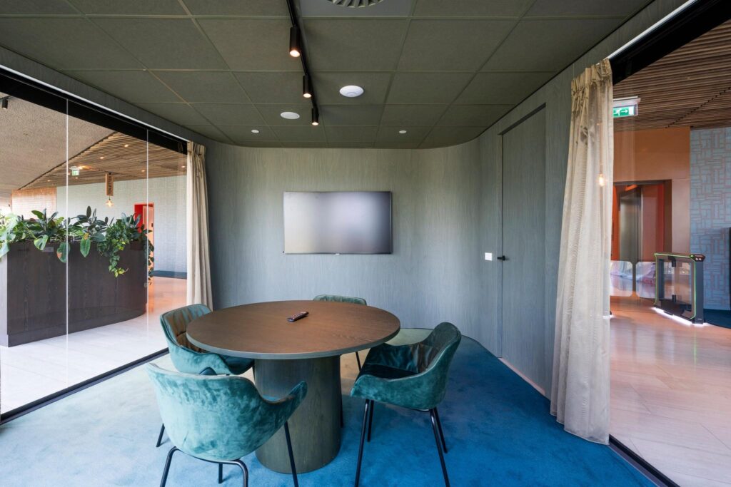 Vergaderruimte aan de David Ricardostraat met ronde tafel, vier stoelen, een flatscreen en uitzicht op een modern kantoorinterieur.